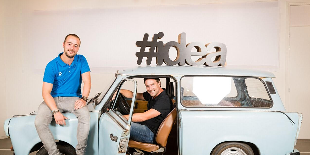 Two men sitting in and on top of a light blue vintage car