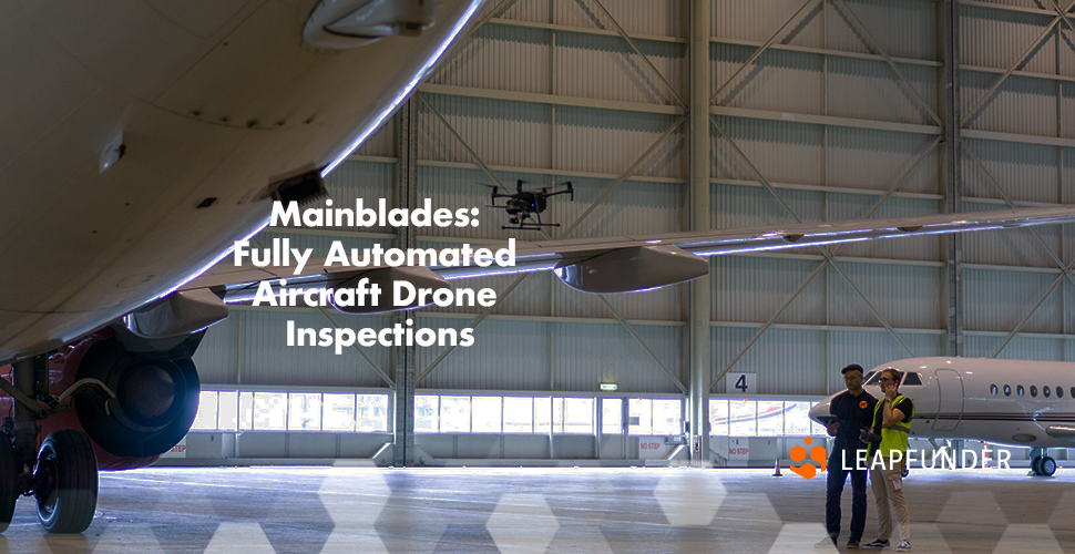 A hangar with aeroplanes and two people inspecting them with a drone